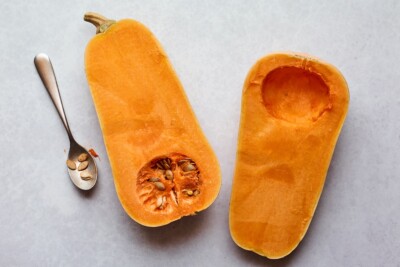 A butternut squash cut in half. One half has the seeds scooped out, the other still has the seeds.