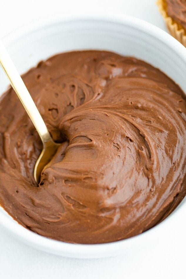 A bowl of healthy chocolate frosting. A spoon is resting inside of the bowl.