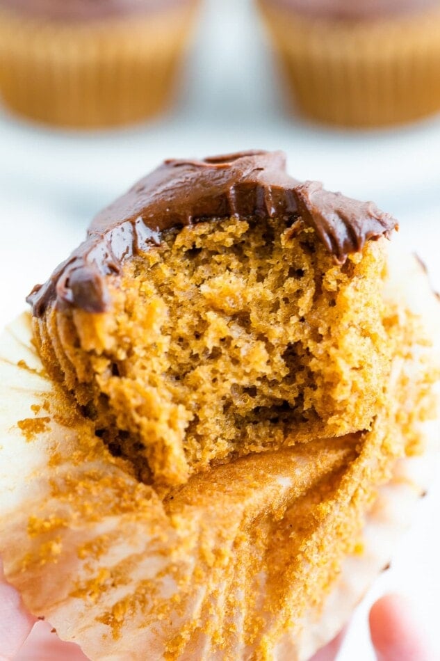 A cupcake with healthy chocolate frosting. The paper wrapper has been pulled down and bite has been taken out of the cupcake.