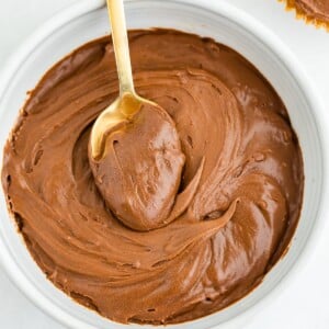 An overhead photo of a bowl of health chocolate frosting. A gold spoon rests inside of the bowl with a scoop of frosting on top of it.