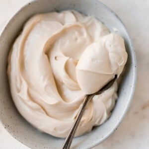 An overhead shot of a bowl of cream cheese frosting. A heaping spoonful is being held overtop of the bowl.