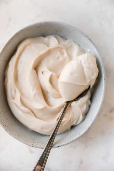 An overhead shot of a bowl of cream cheese frosting. A heaping spoonful is being held overtop of the bowl.