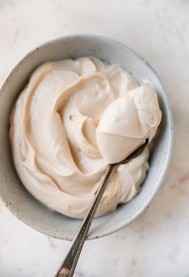 An overhead shot of a bowl of cream cheese frosting. A heaping spoonful is being held overtop of the bowl.