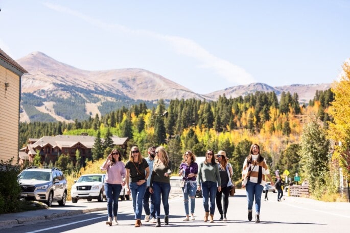 A faraway shot of a group of people walking down a street. There are trees and mountains in the background.