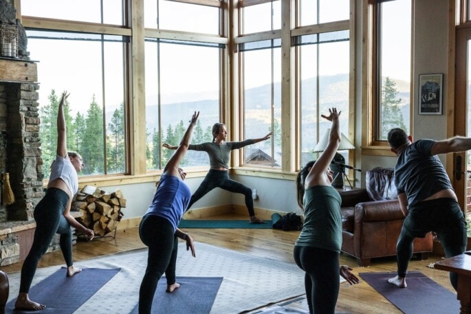 A group of people participating in a yoga class. The instructor is in the center and the participants are mimicking the stretch she is holding.