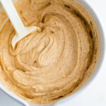 An overhead photo of a mixing bowl with healthy greek yogurt frosting. There is a spatula resting in the bowl.