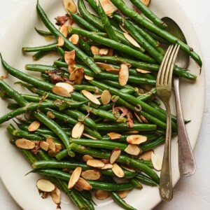 An overhead photo of a serving dish holding green beans almondine. A serving fork and spoon lay across the green beans..