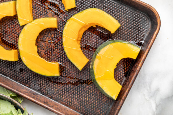 Slices of kabocha squash on a baking pan drizzled with oil.