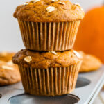 Two pumpkin muffins stacked on top of each other. They are balancing on top of a baking tin.