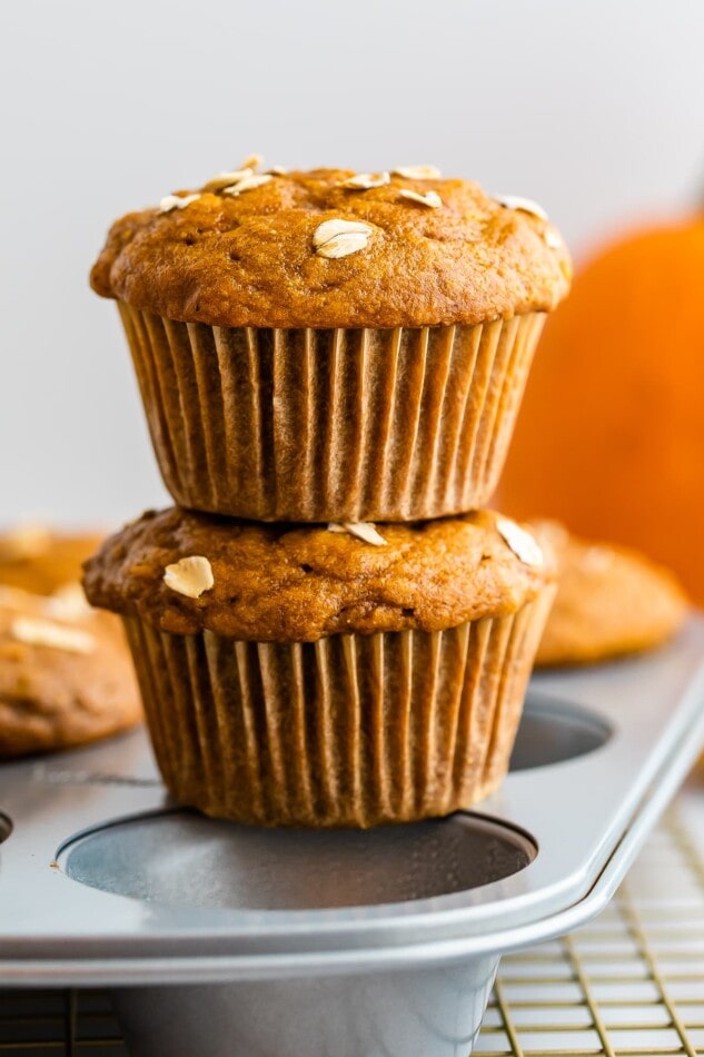 Two pumpkin muffins stacked on top of each other. They are balancing on top of a baking tin.