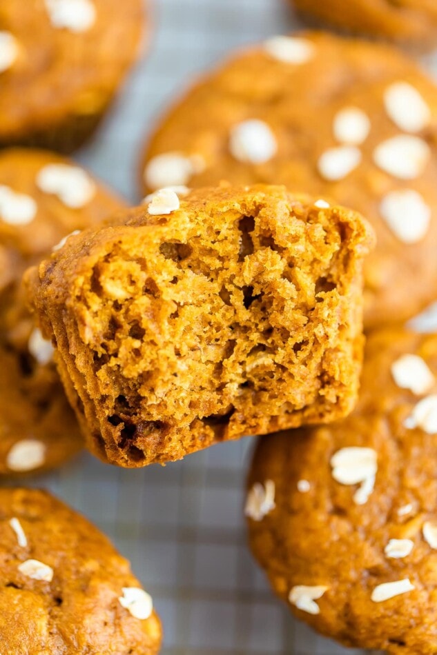 An unwrapped pumpkin muffin with a bite taken out of it resting against other pumpkin muffins.