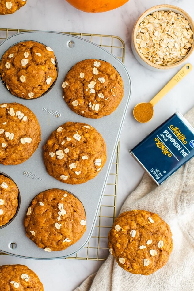 An overhead photo of baked pumpkin muffins in a baking in. A container of Kroger branded pumpkin pie spice is laying next to the tin as well as extra oats and muffins.