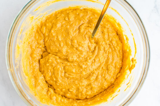 Wet and dry ingredients combine in a mixing bowl. A spoon is sticking out of the mixture and bowl.