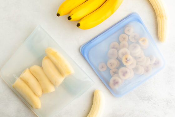 An overhead photo of two stasher bags. In one stasher bag is banana halves and the other has banana slices.