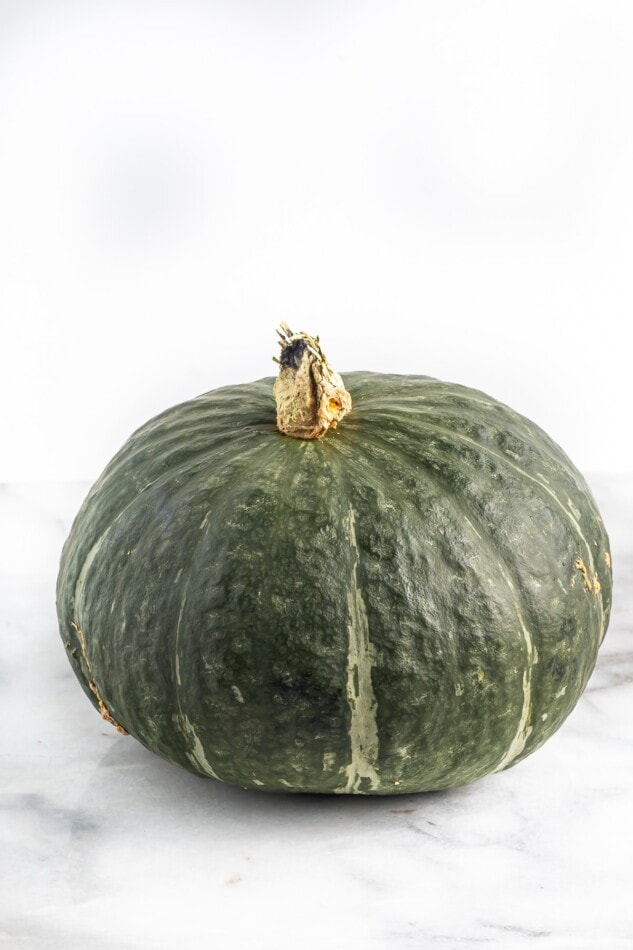 A whole kabocha squash on a marble countertop.