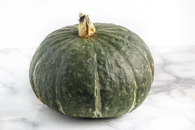 A whole kabocha squash on a marble countertop.