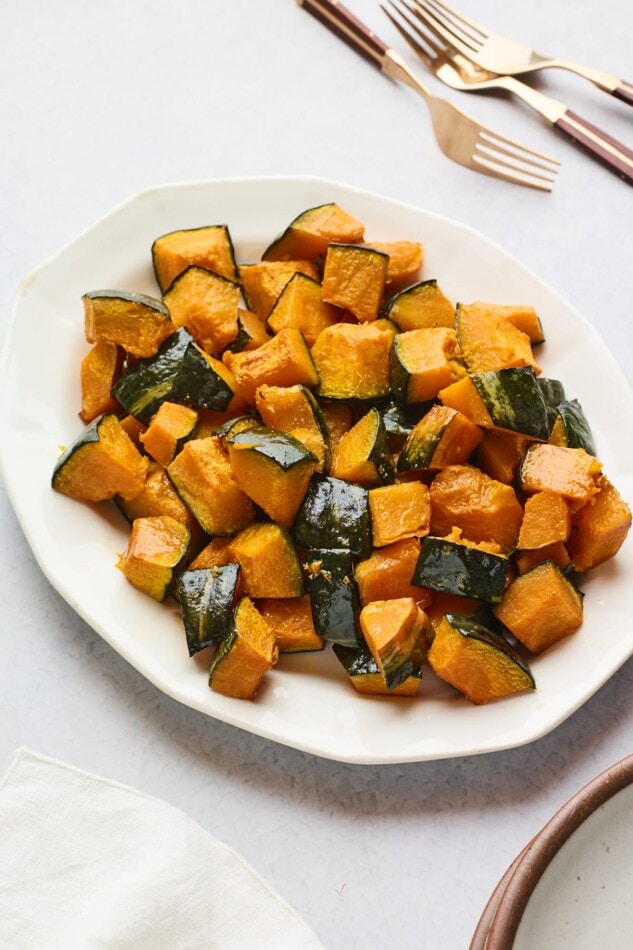 A serving dish full of roasted Kabocha tots. A few forks lay at the top of the frame.