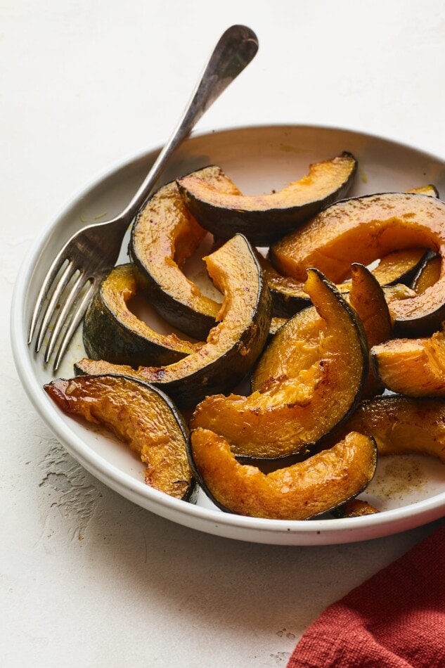 A shallow bowl with slices of cinnamon maple roasted Kabocha squash. A fork rests inside the bowl.