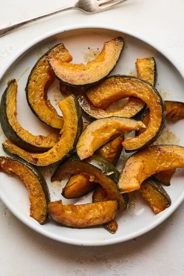 An overhead photo of a plate of cinnamon roasted Kabocha squash slices. A fork rests next to the plate.