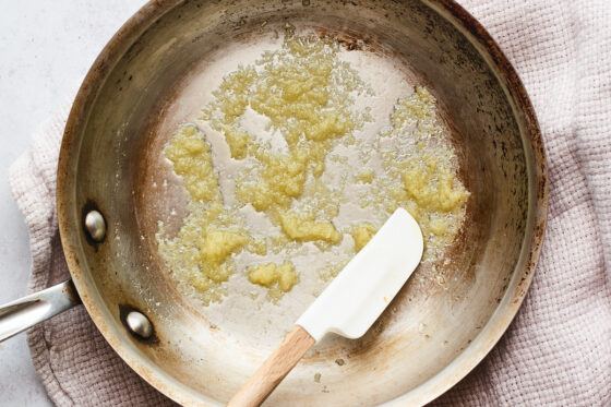 Ghee, garlic, and sea salt sautéd in a saucepan. A small spatula rests on the side of the saucepan.