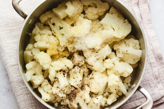 Cooked cauliflower florets in a large pot that has been drained of the water and has spices added.