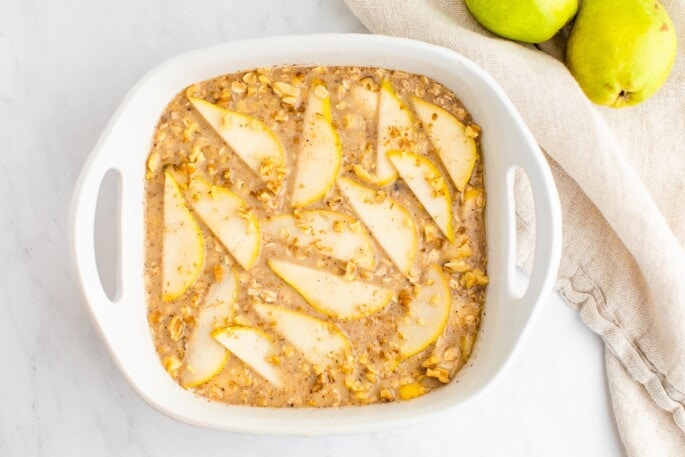 Pear baked oatmeal mixture in a square baking dish topped with slices of pear.