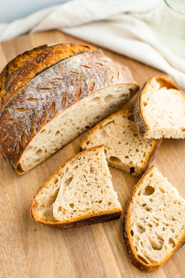 A loaf of sourdough bread sliced open on a wooden cutting board with 2 slices cut in half scattered in front of the loaf.