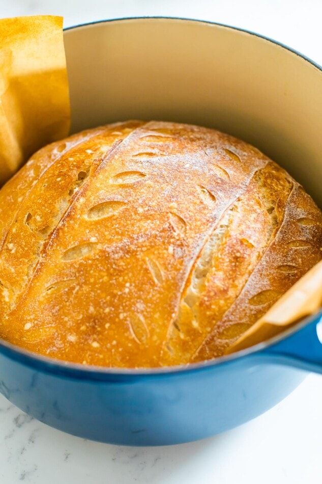 A freshly baked loaf of sourdough bread still in a dutch oven. The top is golden brown.