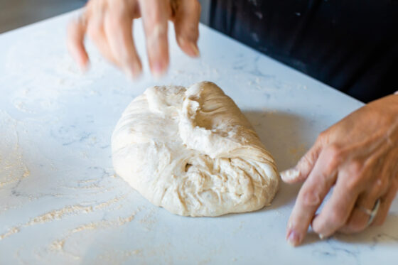 Two hands are seen in action folding bread dough.