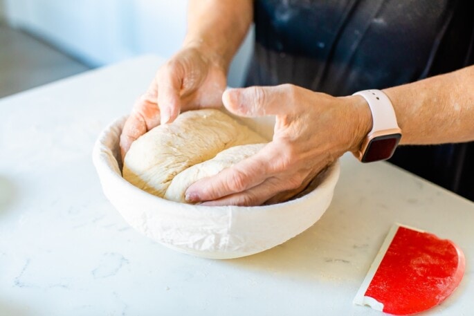 A woman is place a ball of sourdough bread dough into a banneton basket.