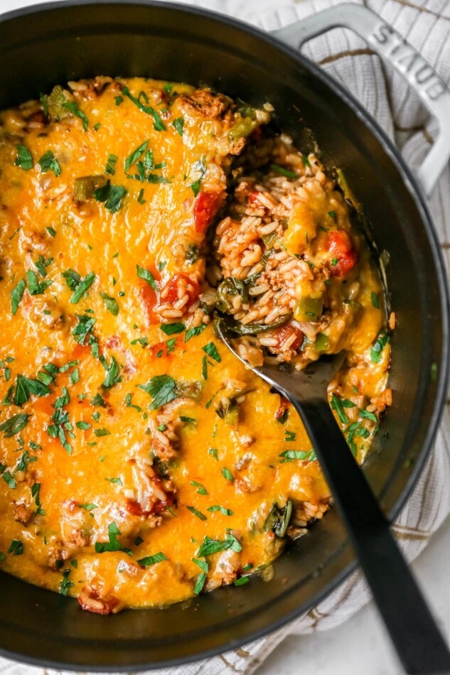 A large pot with stuffed pepper casserole covered in melty cheese. A serving spoon is scooping out a portion of the casserole.