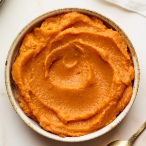 A bowl of sweet potato puree. A spoon is laying facedown next to the bowl.