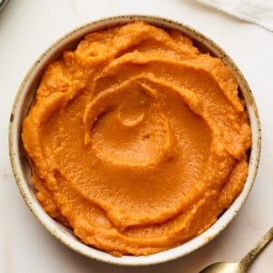 A bowl of sweet potato puree. A spoon is laying facedown next to the bowl.