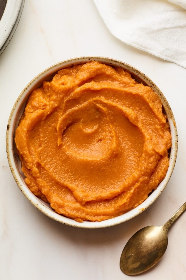 A bowl of sweet potato puree. A spoon is laying facedown next to the bowl.