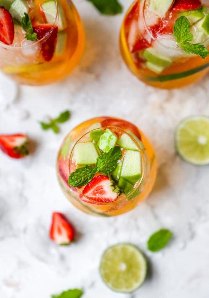 An overhead photo of a glass of white wine sangria with fruit on top. There are two additional glasses cut halfway out of the frame.