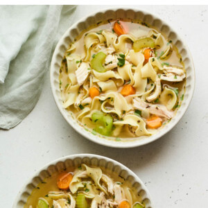 Two bowls of chicken noodle soup. A spoon and a cloth napkin are to the side.