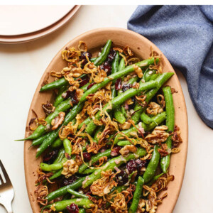 An overhead photo looking down onto a serving dish containing green bean salad topped with fried shallots. A fork is resting next to the serving dish, as well as a blue linen dishcloth.