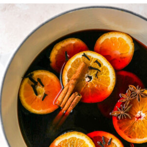 A large pot containing mulled wine with orange slices, cinnamon sticks, cloves and star anise floating in the wine.