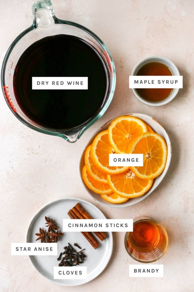 Ingredients measured out to make mulled wine: dry red wine, male syrup, orange, cinnamon sticks, star anise, cloves and brandy.