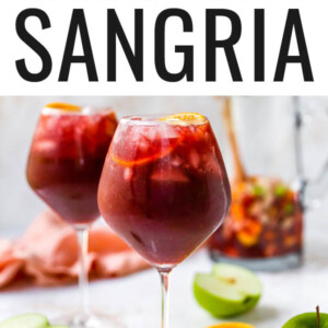 A wine glass containing red wine sangria. There is a second glass out of focus in the background along with a pitcher.