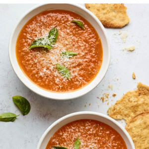 Two bowls containing tomato basil soup. Each bowl is topped with fresh basil leaves.