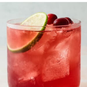 A closeup photo of a short glass filled with vodka cranberry over ice and topped with a slice of lime and a few whole cranberries.