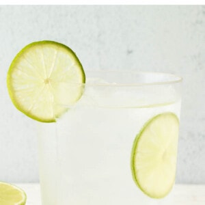 A drink glass containing vodka soda. A slice of lime is in the glass and another on the rim.