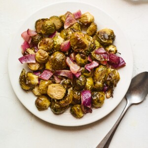 An overhead photo looking down on a plate of apple cider vinegar roasted Brussels sprouts. A silver spoon is laying next to the plate.