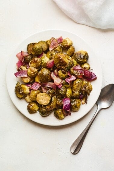 An overhead photo looking down on a plate of apple cider vinegar roasted Brussels sprouts. A silver spoon is laying next to the plate.