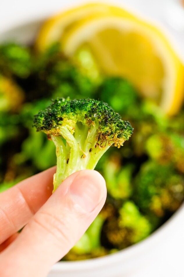 A hand holding up a piece of air fried broccoli.
