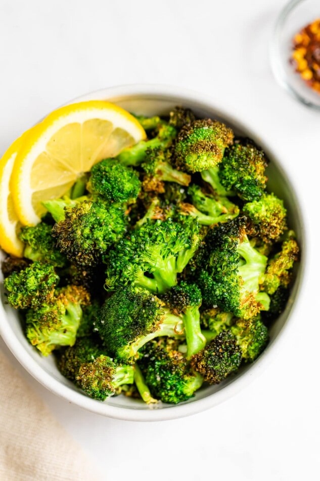 An overhead view of a small bowl of air fryer broccoli. There are two lemon slices resting in the bowl as a garnish.
