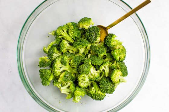 A mixing bowl containing broccoli florets that have been tossed with olive oil, salt, pepper and garlic powder.