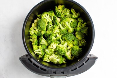 An air fryer basket containing broccoli florets before cooking.
