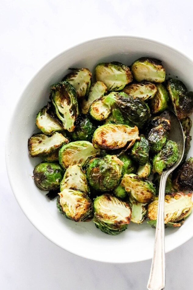 A closeup photo of air fried brussels sprouts in a bowl. A serving spoon rests in the bowl.